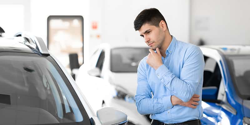 A man in a blue shirt examines a car, showcasing his interest in the vehicle.