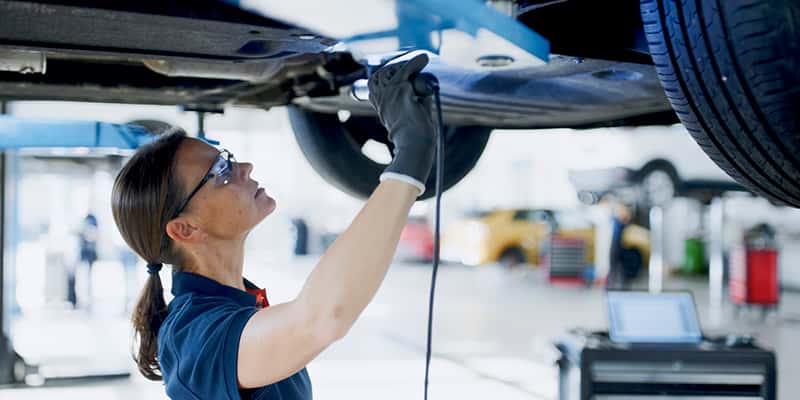 A woman in a garage is engaged in vehicle maintenance, surrounded by tools and automotive equipment.