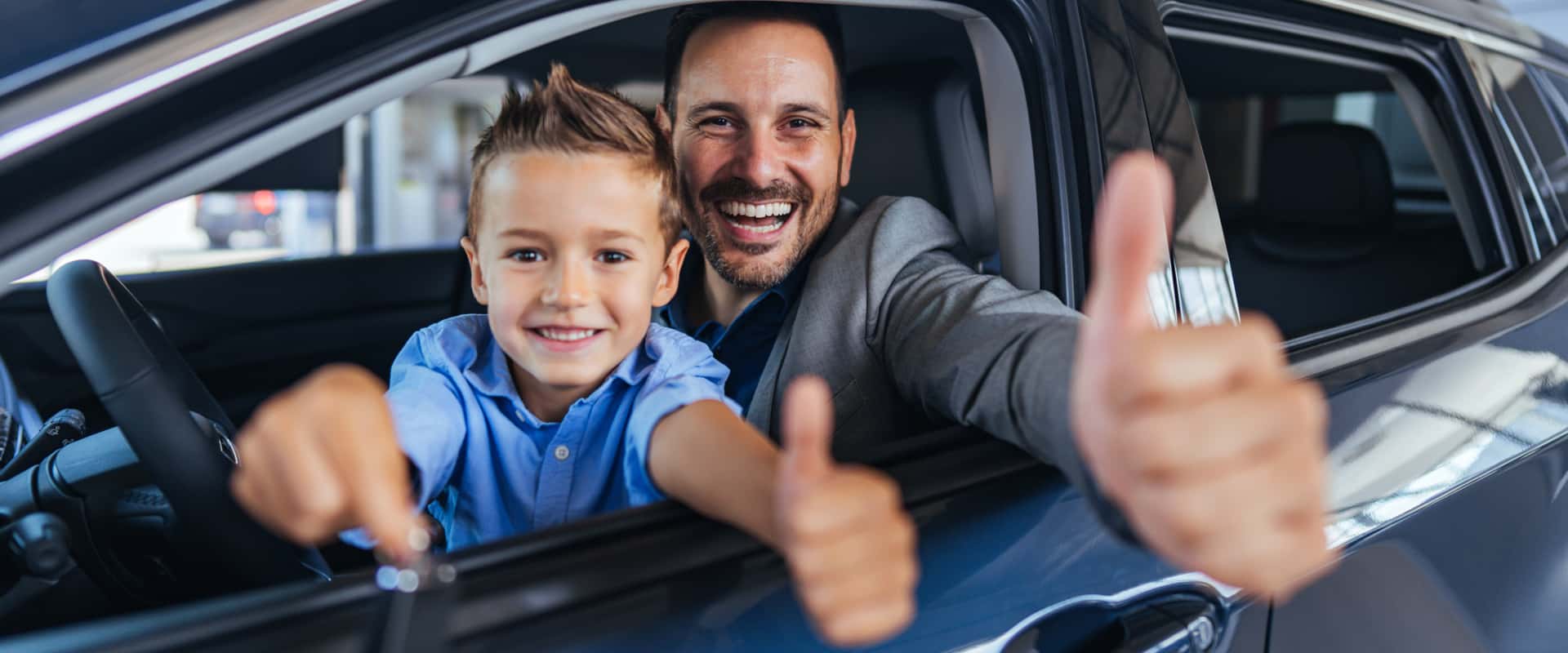 A man and a boy in a car smiling and giving thumbs up, expressing joy and approval.