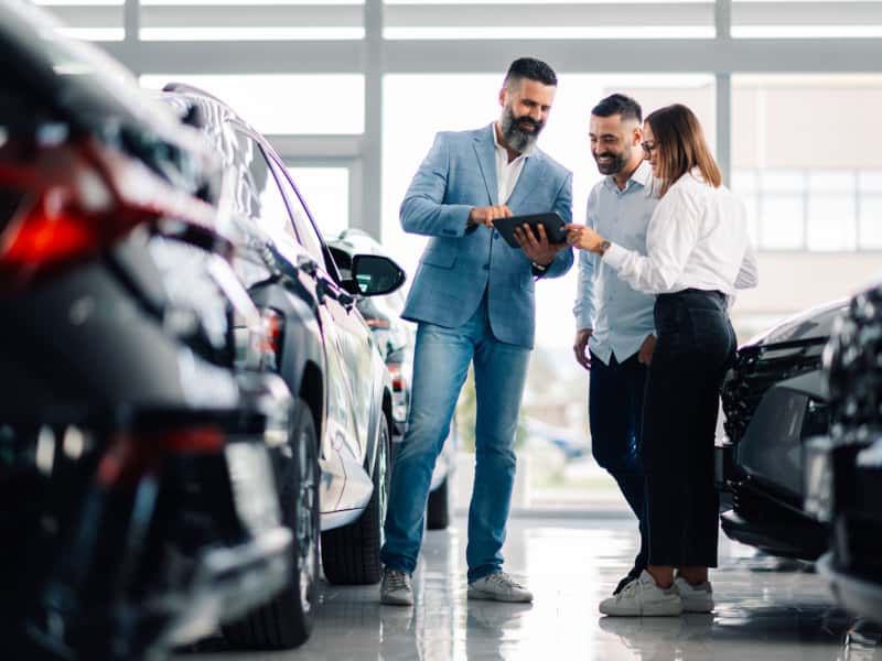 Two men and a woman examining a car in a modern showroom setting.