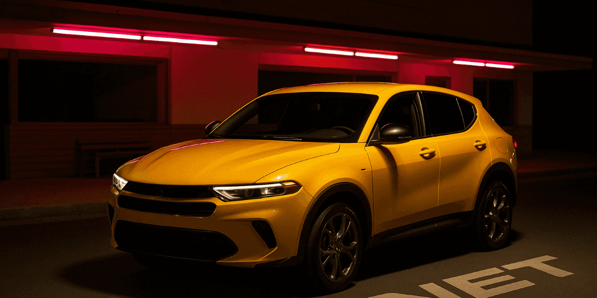  Yellow 2025 Dodge Hornet under pink neon lights with “HORNET” lettering on the street, captured from a dynamic three-quarter angle.