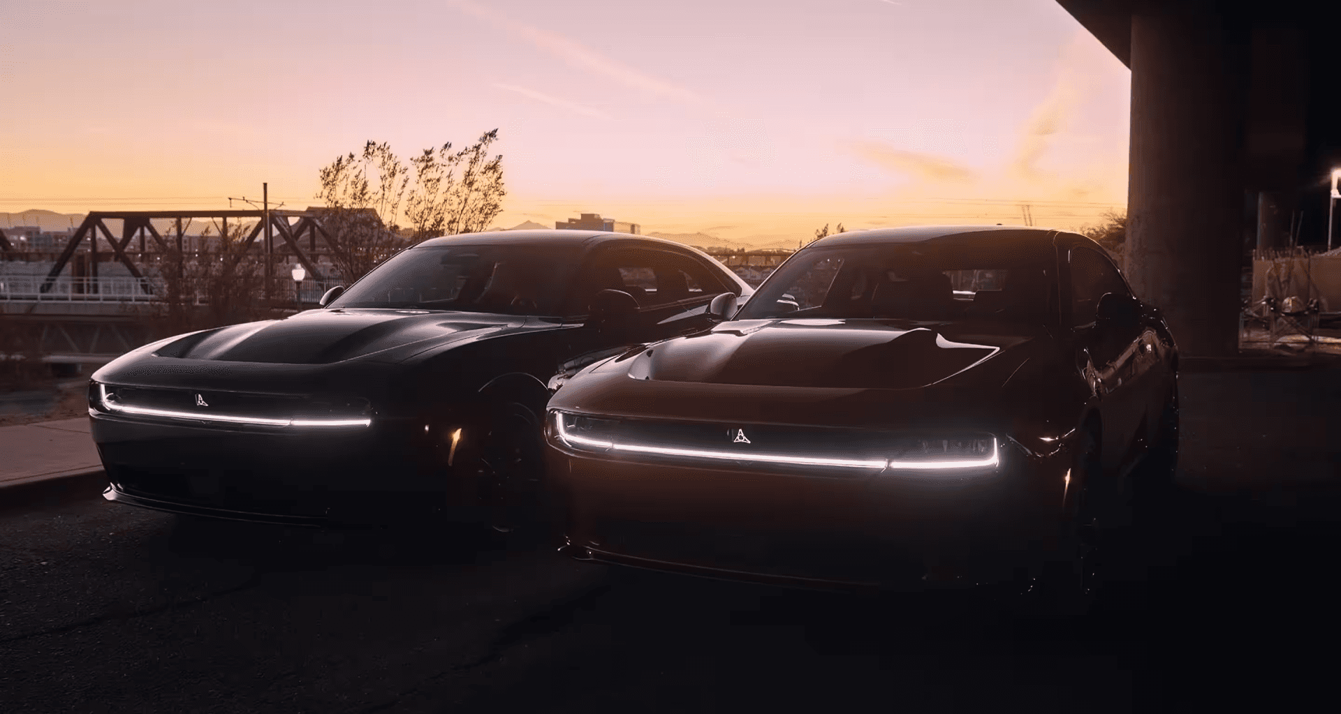 Two 2025 Dodge Charger Daytona models with illuminated front LED light bars parked side by side at sunset, showcasing bold styling and electric performance, available at Helfman Dodge Chrysler Jeep RAM FIAT.