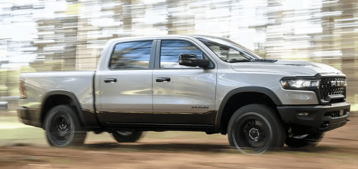 2025 RAM 1500 pickup truck in silver driving through a lush green countryside, highlighting its refined power and rugged versatility.