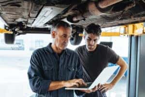 Two male mechanics at Helfman Dodge doing an inspection under a vehicle.