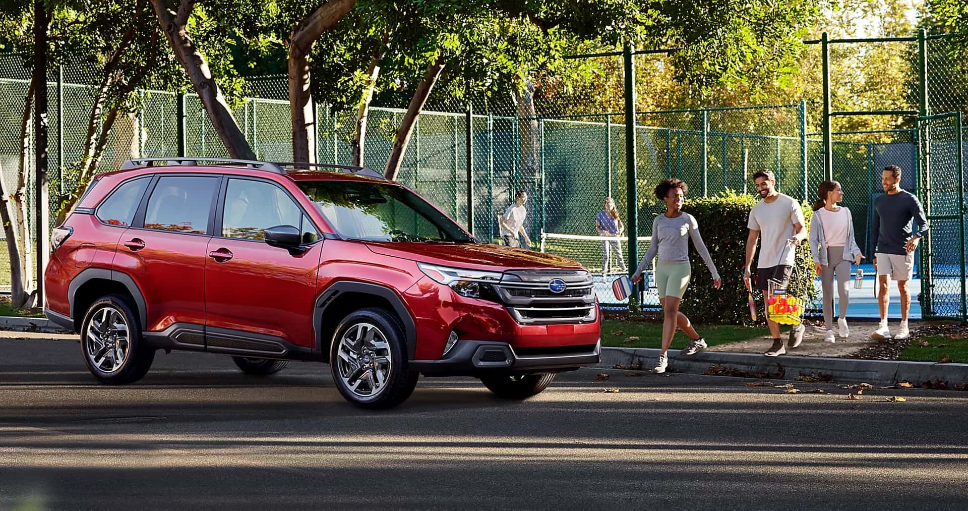Red Subaru Forester parked in front of a tennis court.