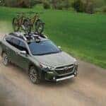A green Subaru Outback driving down a dirt road with a bike on the roof