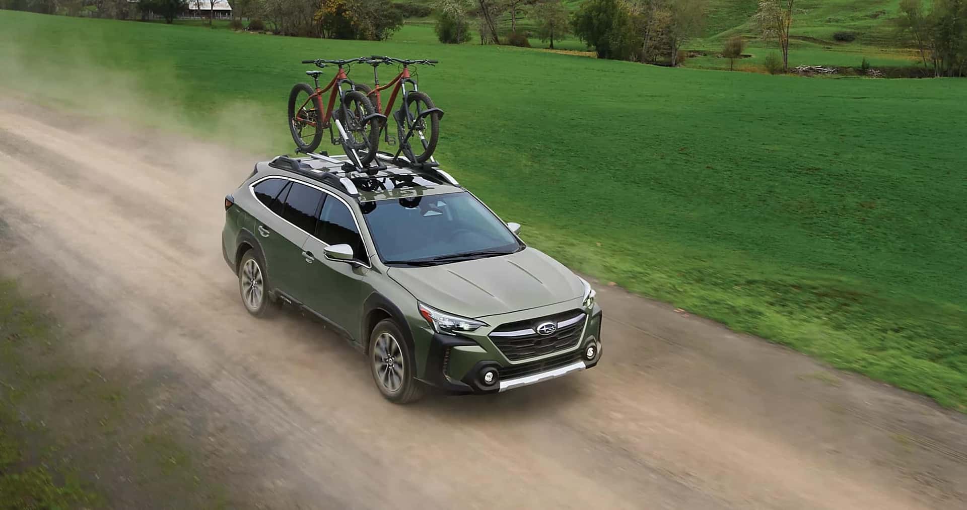 A green Subaru Outback driving down a dirt road with a bike on the roof
