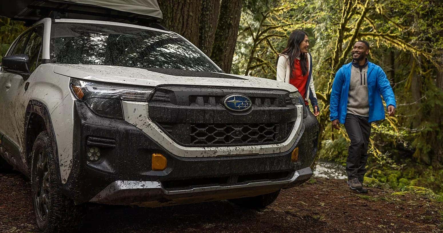 A couple walking at a campsite in a 2026 Subaru with a Camping Tent on the roof.