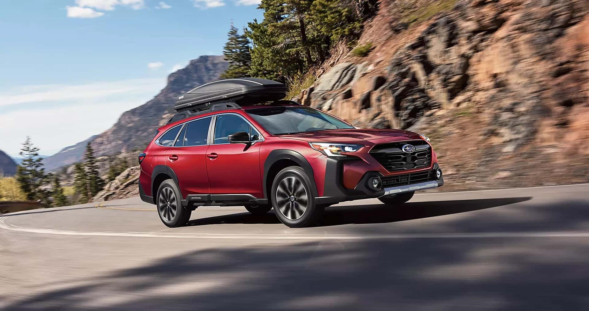 a red Subaru Outback driving down the road with a cargo rack on top.