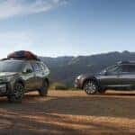 Three Subarus parked on a hill overlooking the mountains.