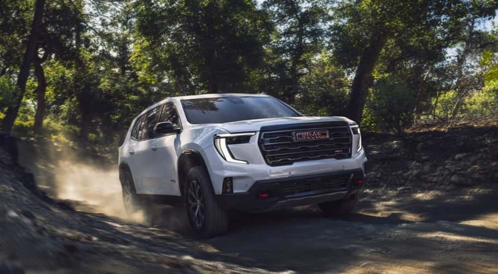 A white 2024 GMC Acadia AT4 driving to a used GMC dealer.