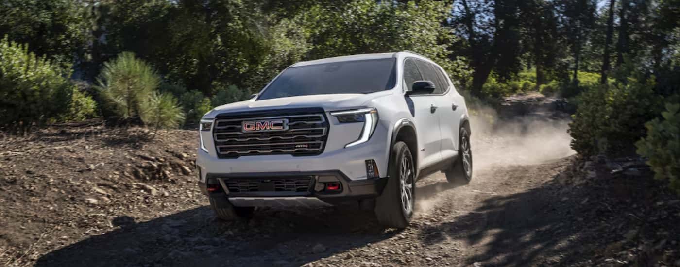 A white 2025 GMC Acadia AT4 off-roading on a dirt trail