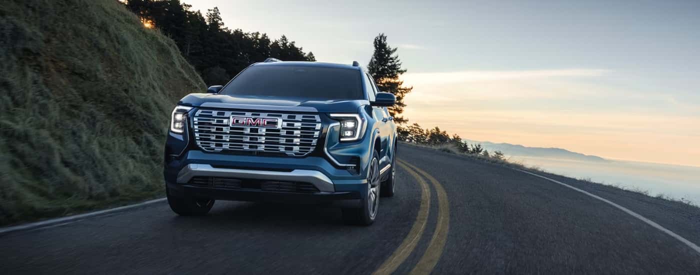 A blue 2026 GMC Terrain driving down a rural road
