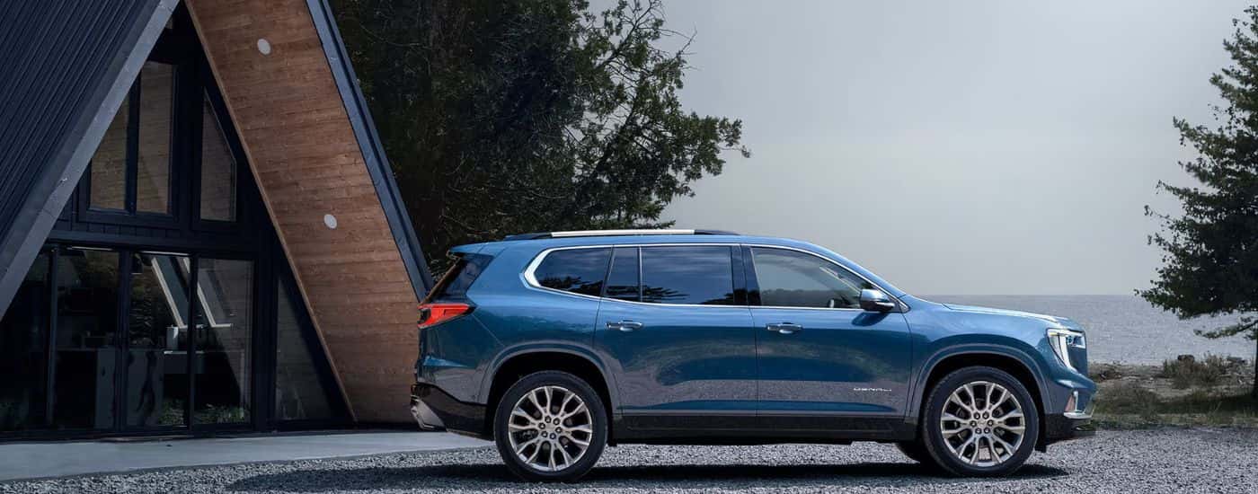 Blue 2026 GMC Acadia Denali parked in front of a lakeside cabin