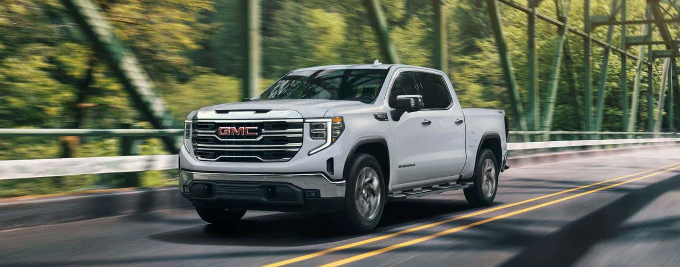White 2026 GMC Sierra 1500 driving across a sunlight bridge.