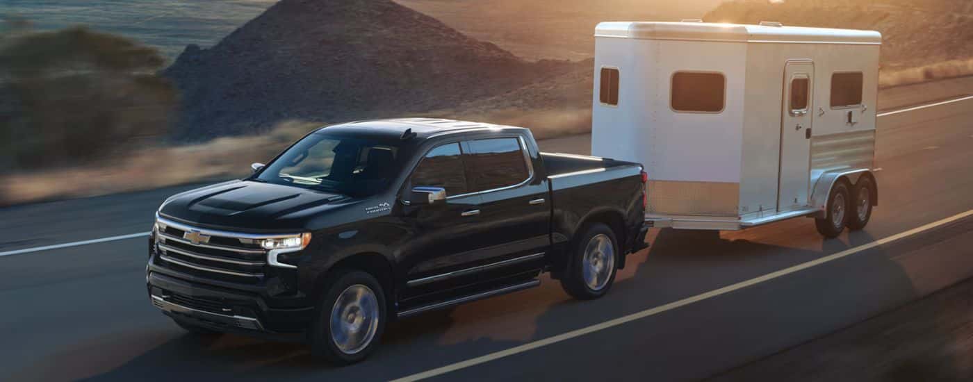 Black 2026 Chevy Silverado 1500 towing a trailer down the road.