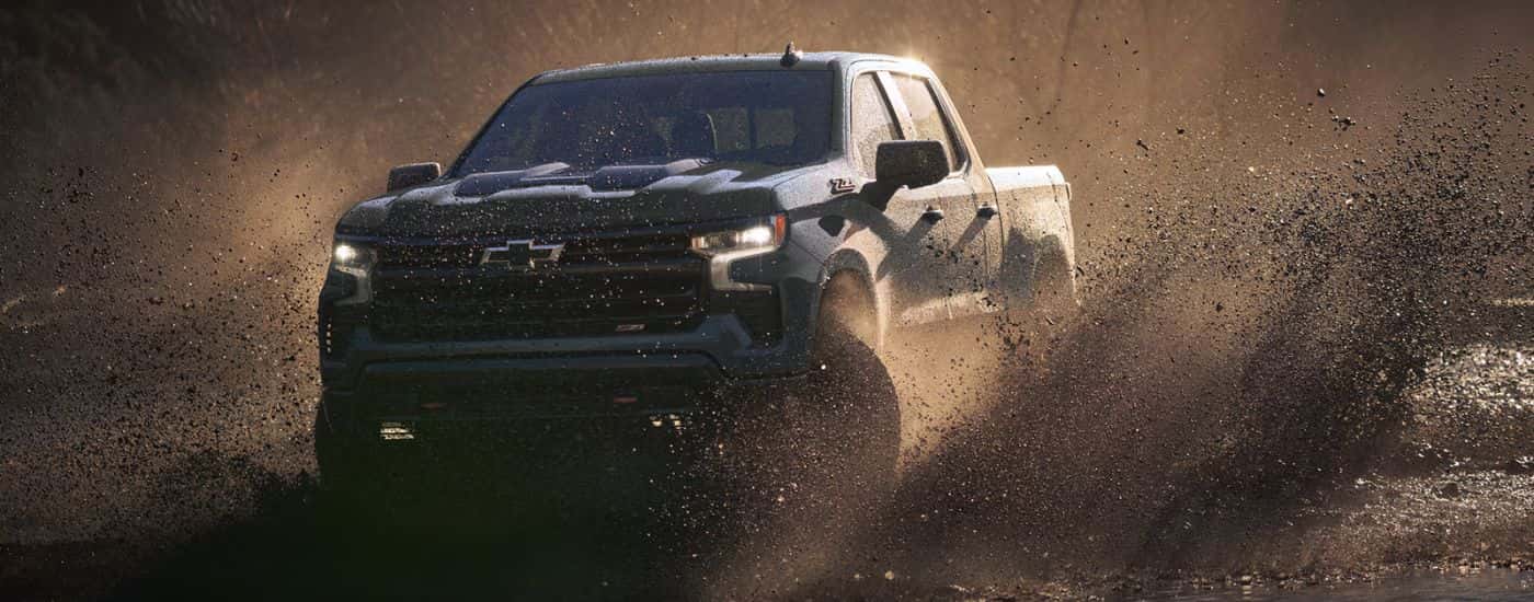 Blue 2026 Chevy Silverado 1500 driving through mud.