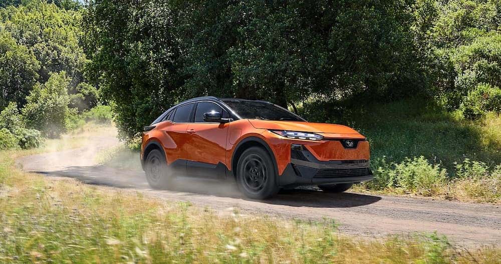 An orange 2026 Subaru Uncharted SUV driving down a tree-lined road