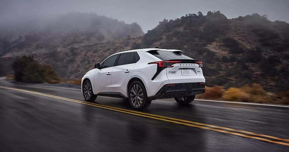 A white 2026 Subaru Solterra SUV driving along a wet, foggy mountain road