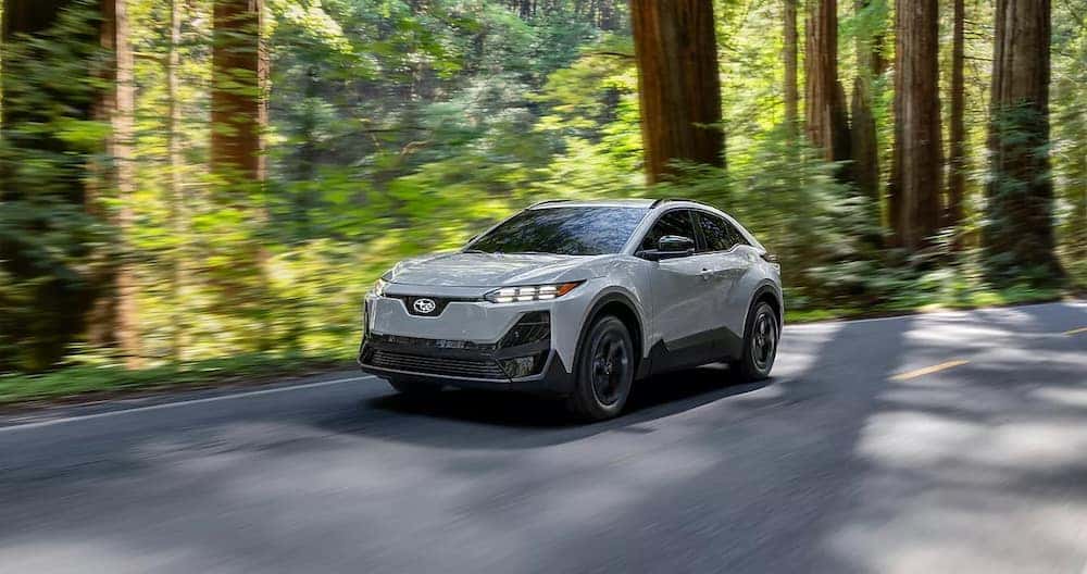 A gray 2026 Subaru Uncharted electric SUV driving down a wooded road