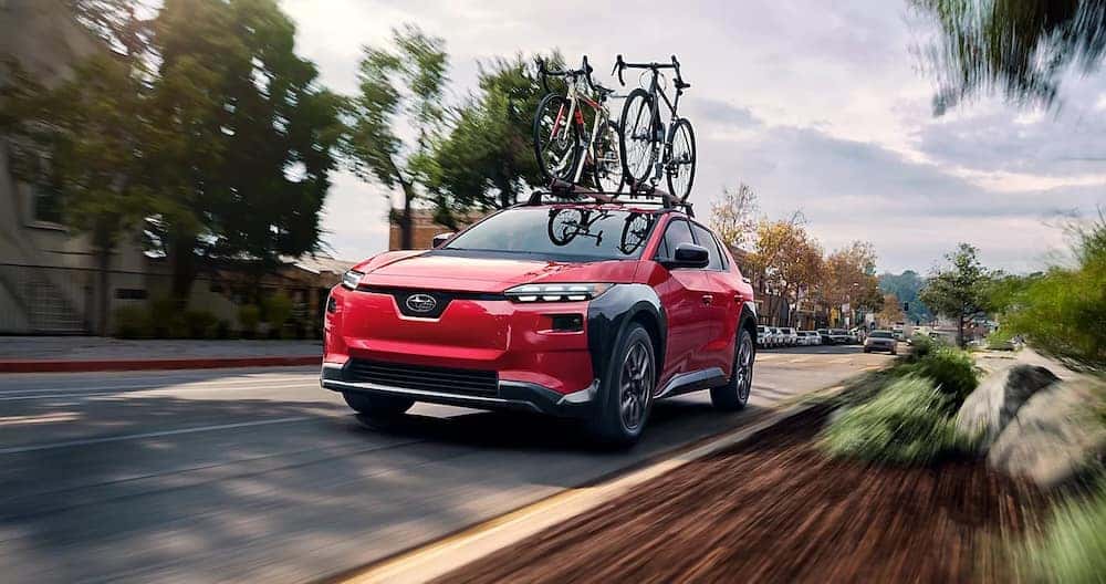 A red 2026 Subaru Solterra with bicycles on its roof rack driving down a city street