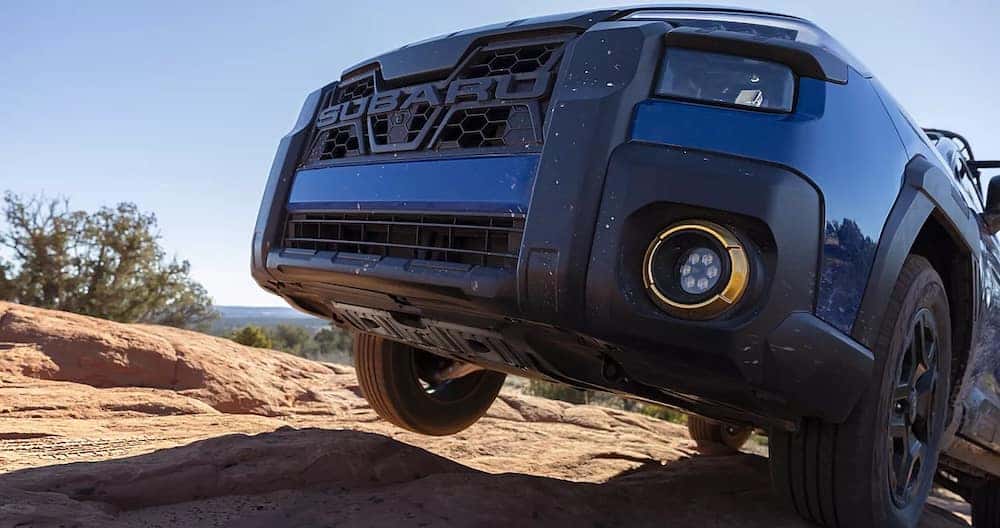 A closeup of the front of a dark blue 2026 Subaru Outback driving up a rocky incline