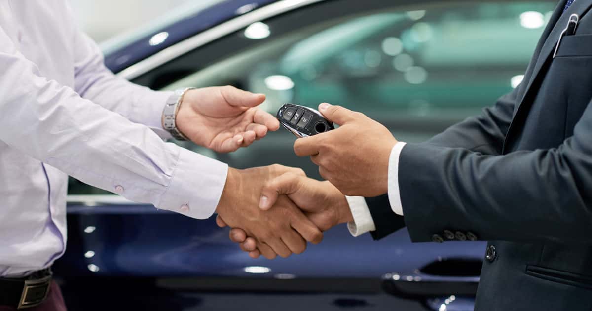 Two pairs of hands exchange a pair of car keys at a dealership