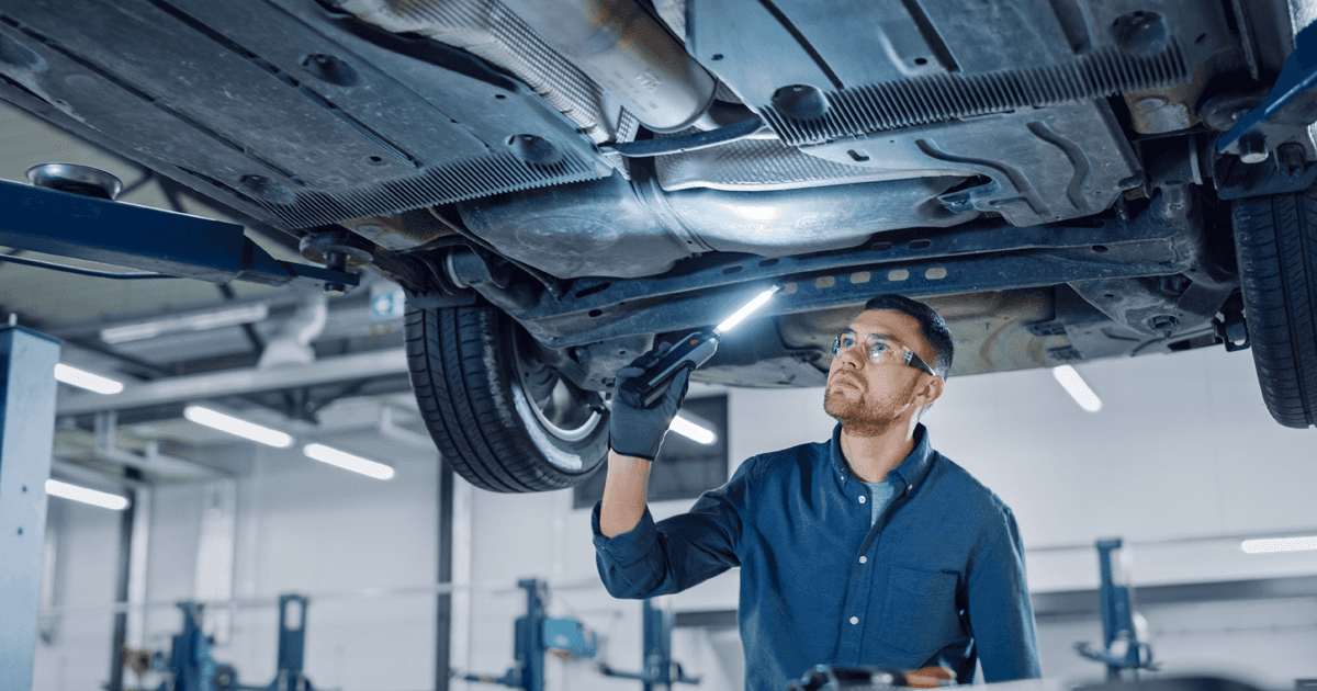 A Service Technician under a vehicle in the service center inspecting the underside of the vehicle.
