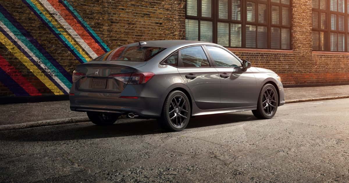 A gray Honda Civic sedan parked infront of an artistic brick building.
