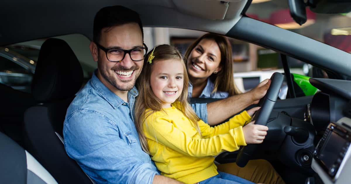 A smiling family sitting in a vehicle at the car dealership.