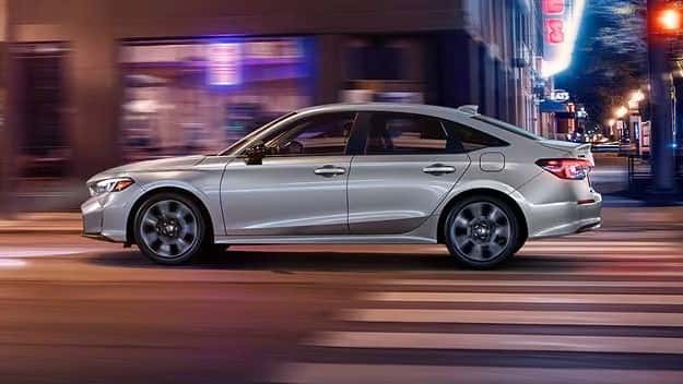 2026 Honda Civic Sport Touring Hybrid sedan driving through a city street at night