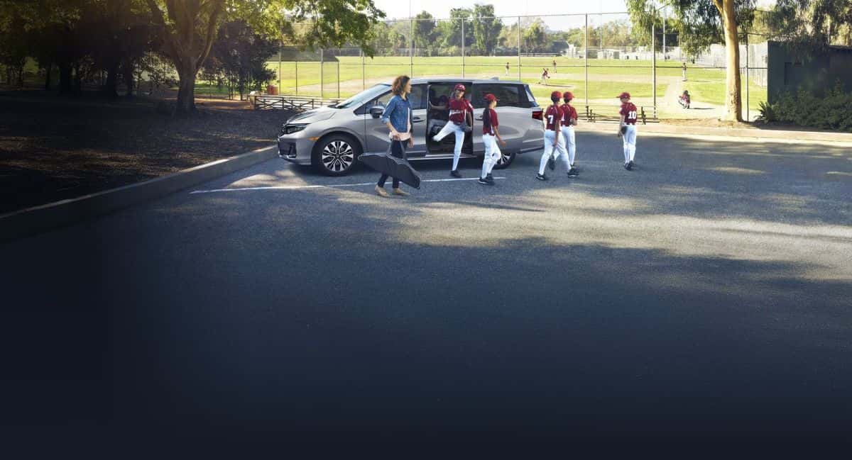 2026 Honda Odyssey parked near a baseball field with a mother and kids in uniform walking toward the sliding door