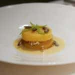 stacked yellow squash with seeds on top, surrounded by yellow sauce