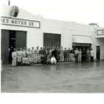 A team of members posing for a photograph in front of the Huffines dealership in 1957, captured in black and white.