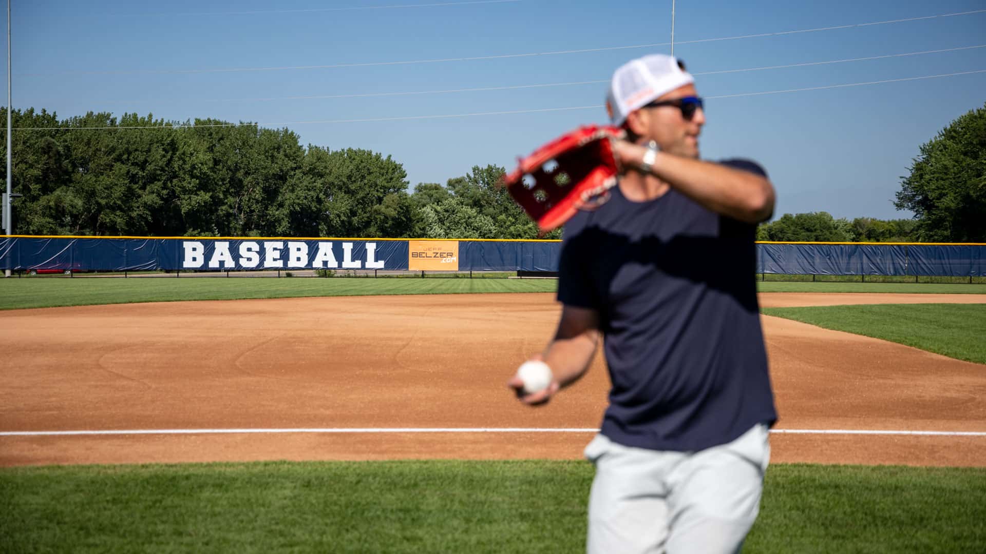 Jeff Belzer throwing a baseball with the Belzer Stadium field behind him