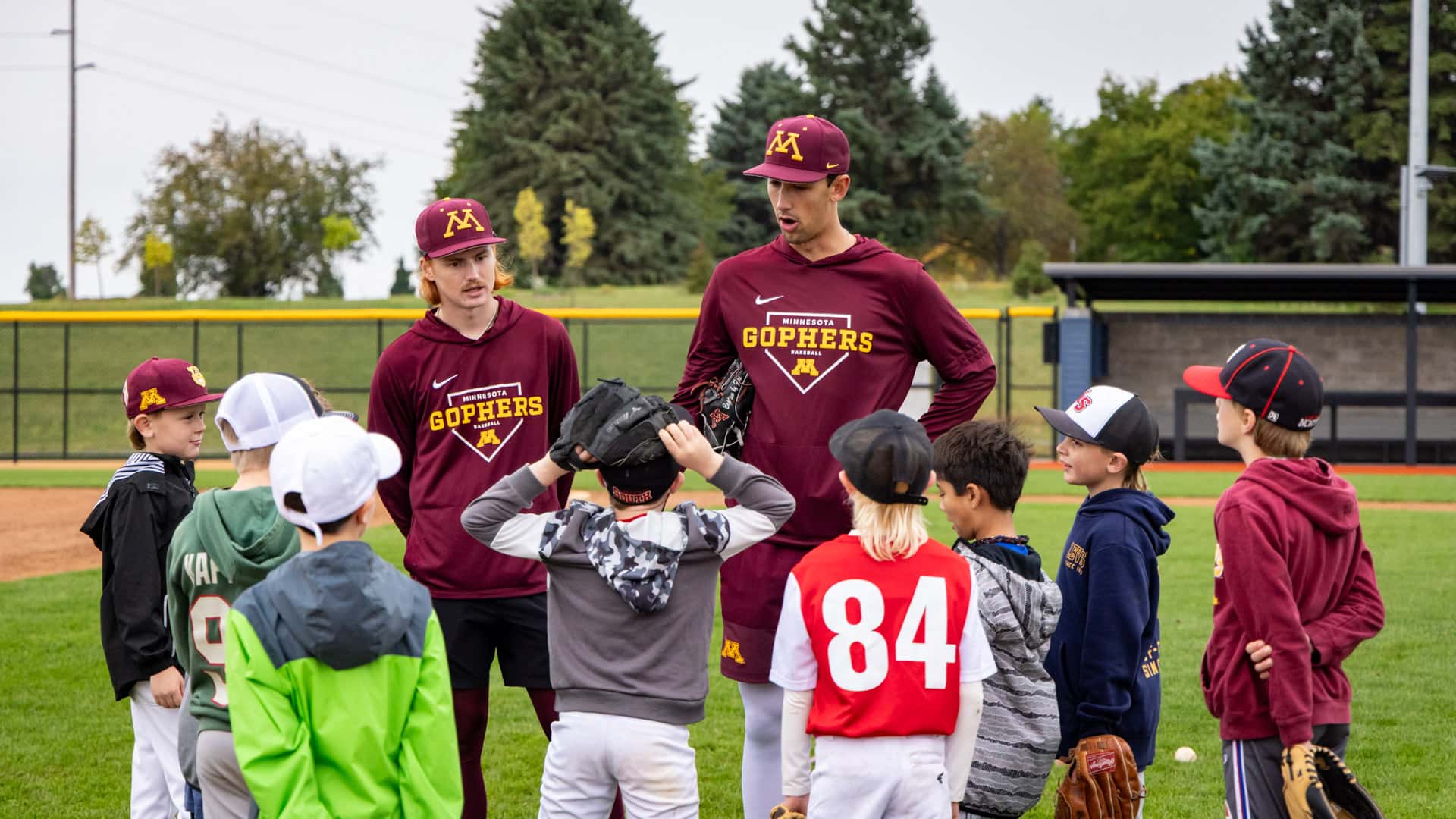 Young campers listening to two Gopher Baseball players during the youth clinic at Belzer Stadium