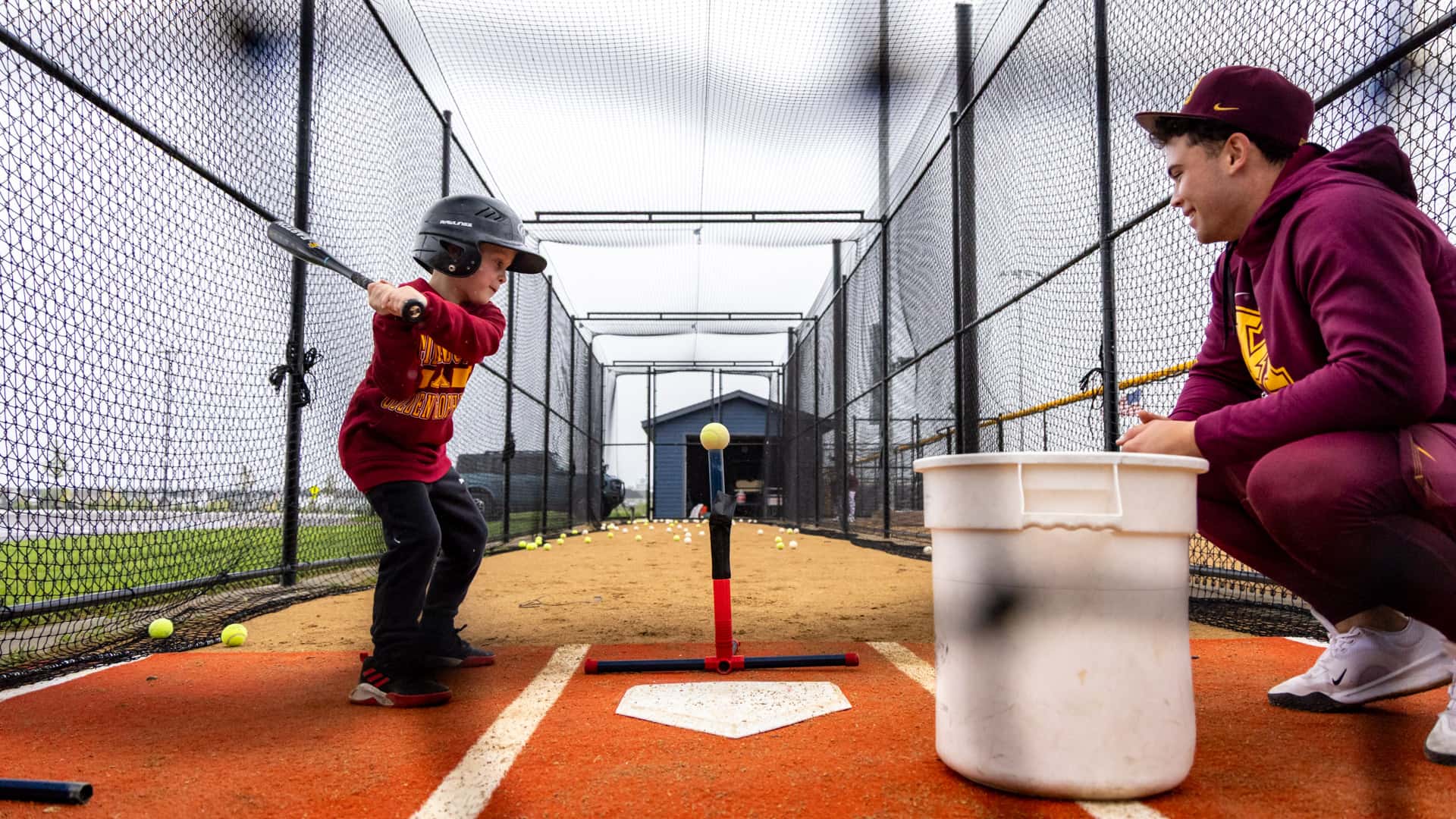 Gopher Baseball player mentoring a young camper during a hitting drill