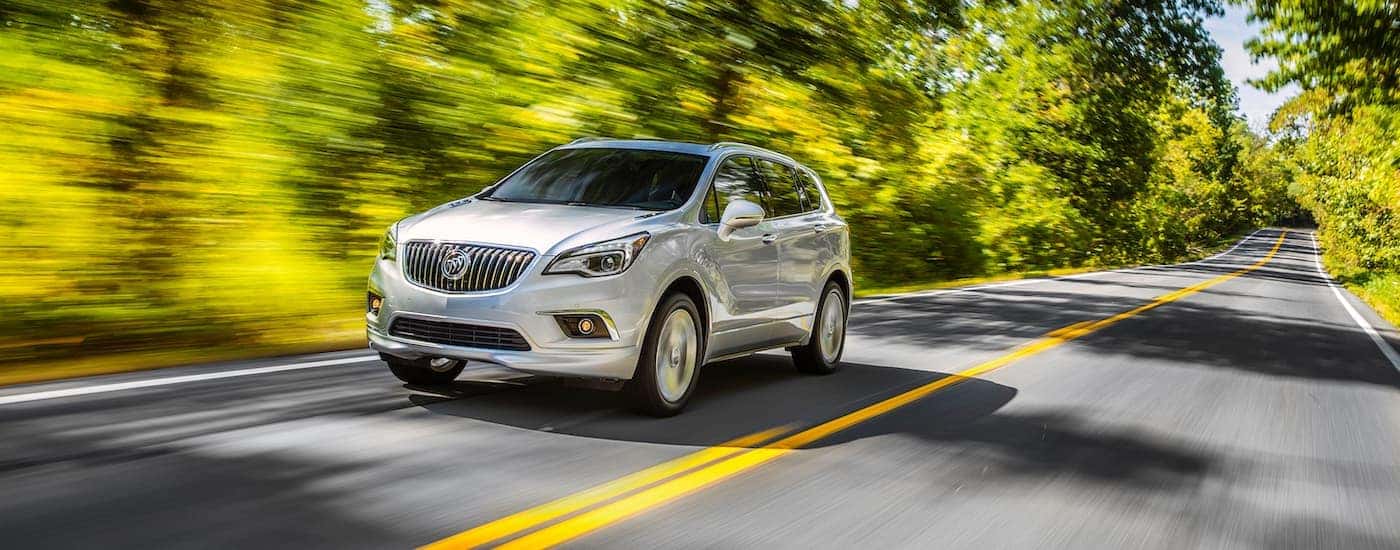 A silver 2017 Buick Envision is shown driving on a tree-lined road after leaving a used Buick dealer in Atlanta.