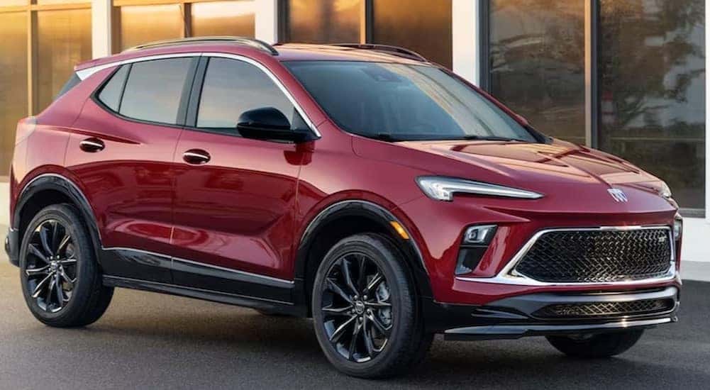 A red 2024 Buick Encore GX Sport Touring is shown parked near a building with glass windows.