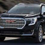 A black 2024 GMC Terrain is shown driving on a highway to a GMC dealer near me.