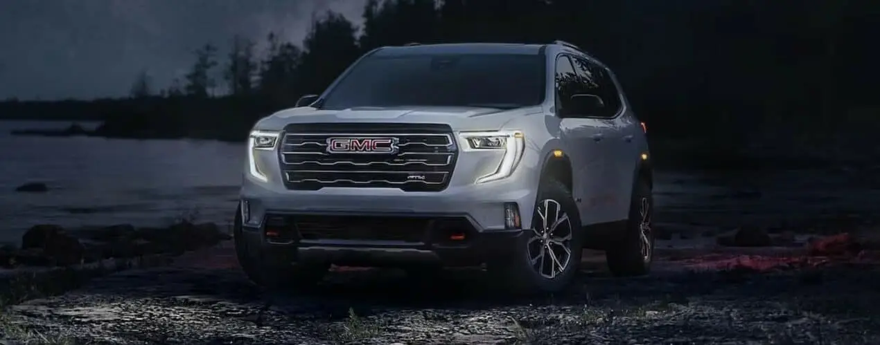 A silver GMC Acadia AT4 is shown parked off-road at night.