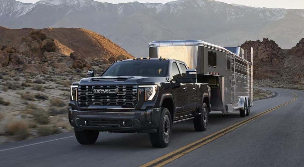 A black 2024 GMC Sierra 3500 HD is shown towing a trailer on a highway.