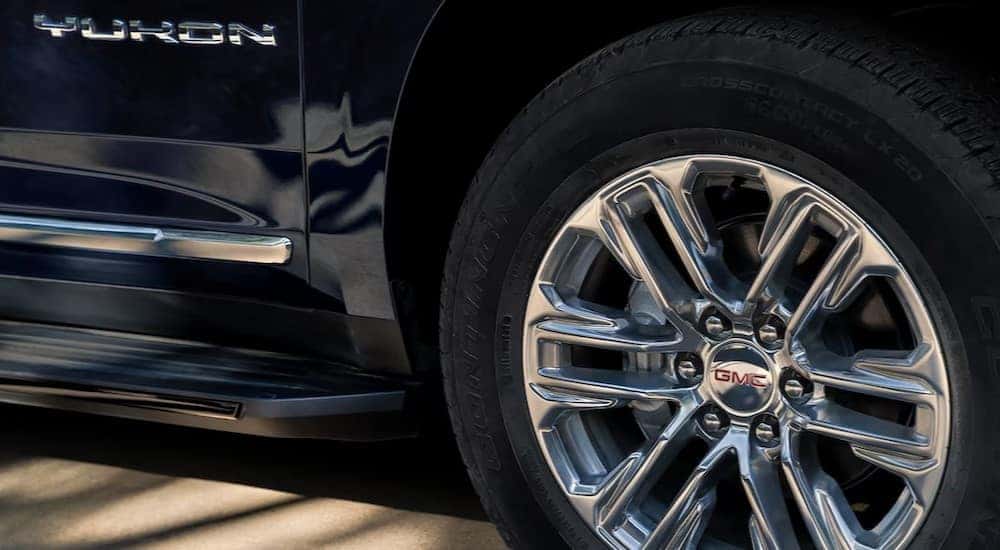 A close-up of a wheel and Yukon badge is shown on a black 2024 GMC Yukon XL.