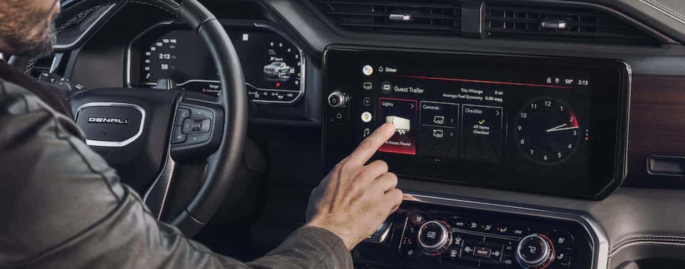 A person is shown pressing a button on the dashboard of a 2023 GMC Sierra 1500 Denali.