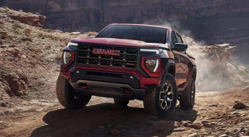 A red 2024 GMC Canyon AT4X is shown driving on a dusty trail.