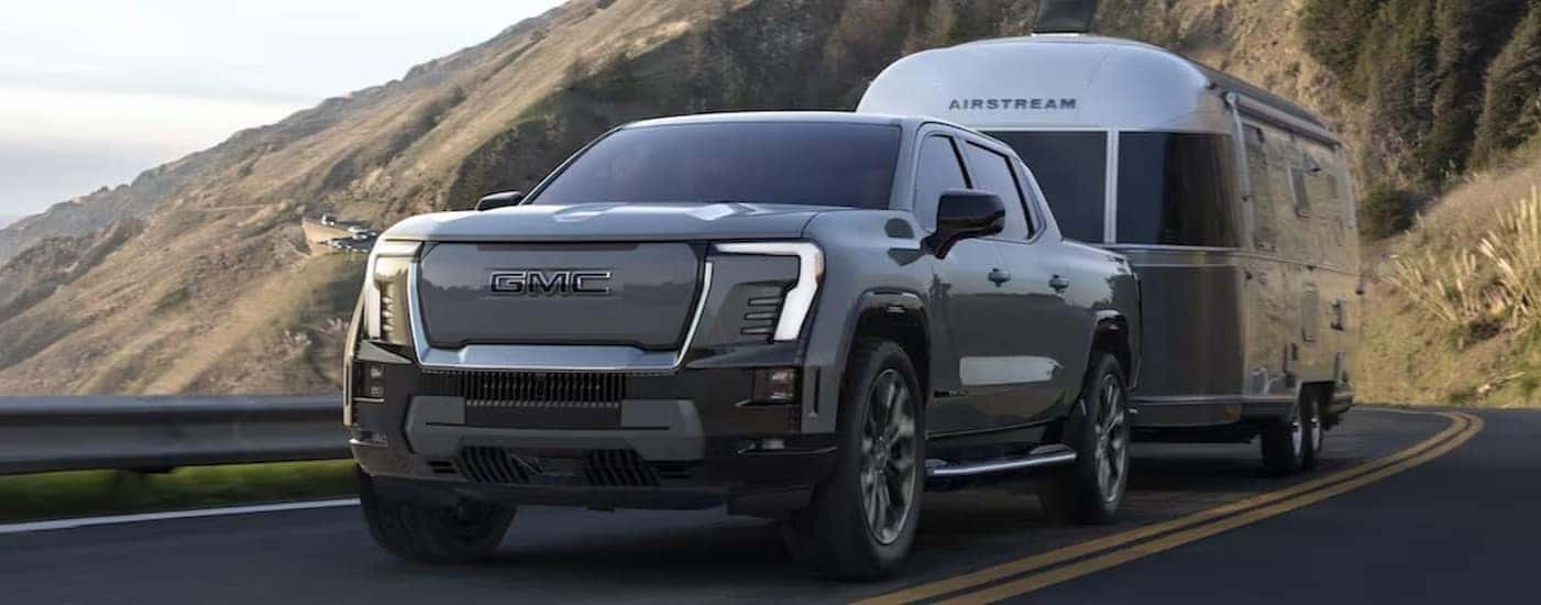 A gray 2024 GMC Sierra EV Denali Edition 1 is shown towing a trailer.