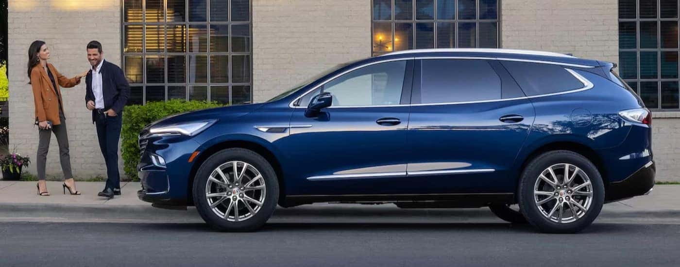Two people are shown standing near a blue 2024 Buick Enclave.