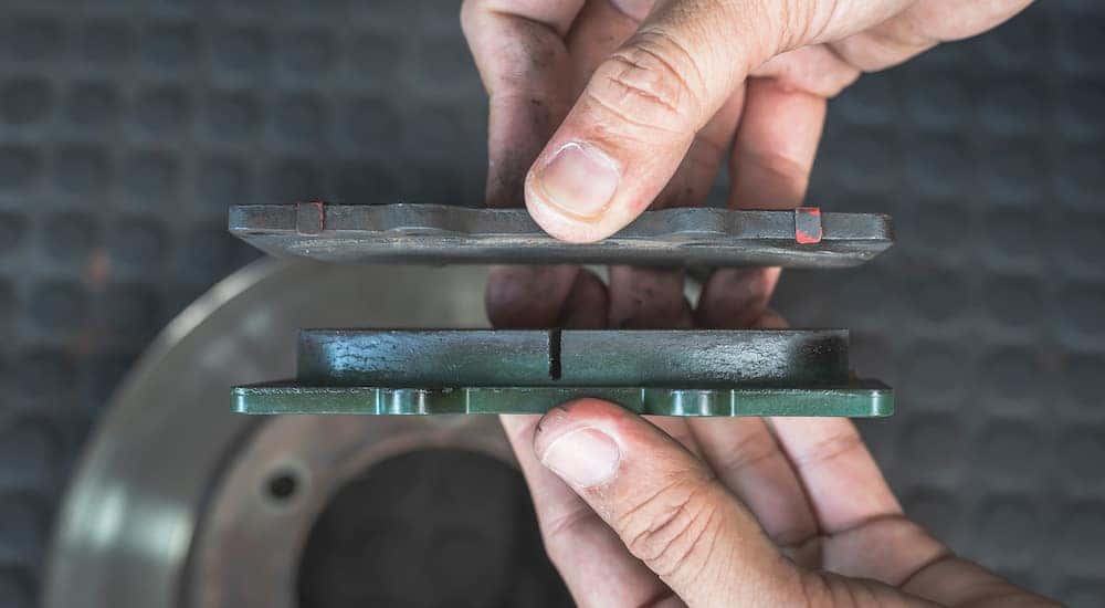Close-up of a mechanic holding a new brake pad next to an old, worn brake pad.
