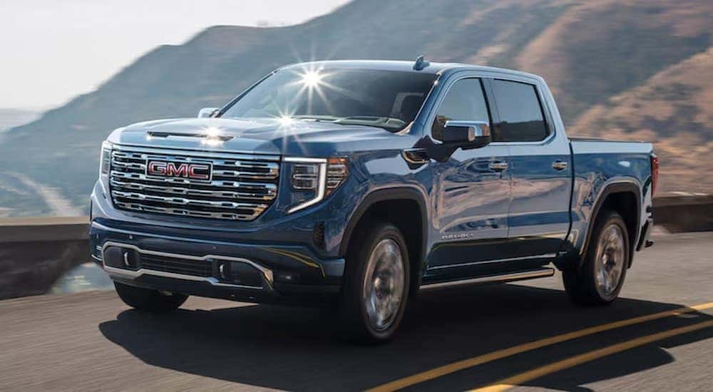 A blue 2024 GMC Sierra 1500 Denali is shown driving on a highway after viewing trucks for sale.