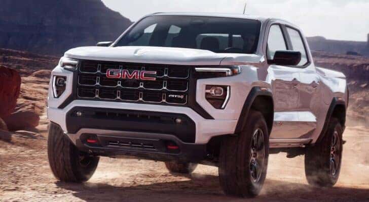 A white 2024 GMC Canyon AT4 off-roading in a dusty area.